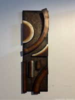 Front view of abstract rectangular metal art piece with various geometric 3D shapes in brown, gold, and silver.