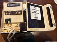 Muscle exercise stimulator electronic unit with knobs and cables inside open grey vinyl case along with guide booklet
