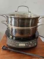 Photo of assembled induction cooktop with stainless steel pot, steam basket, and glass lid stacked.