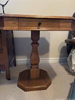 Front view of heavy oak games table showing the single pedestal base, octagonal platform, and drawer with knob.