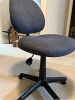 Medium blue office chair with dark fabric, showing the side view with the lever for hydraulic height adjustment and the five-legged base with metal casters.