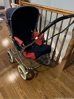 Side view of Prego baby stroller showing blue and red padded seating, metal frame, large white wheels and wire under basket.