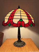 Full view of lamp showing stained glass shade with red, cream, and green colors, lit and unlit conditions.