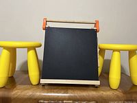 Front view of two yellow toddler stools with black chalkboard between them on wooden surface.