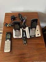 Three VTech cordless phones on wooden surface, two on charging bases with cables, one cordless without base, also showing cables.
