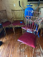 Four gold metal chairs with red seat cushions showing wear and paint peeling, arranged on a wood floor with background exercise equipment.