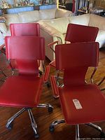 Four red swivel office chairs shown together with chrome metal bases and padded armrests.