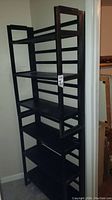 Full view of folding black wood shelf unit showing its height and multiple shelves.