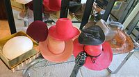 Photo showing a variety of ladies hats on display including red, pink, orange, beige, gray, black, and brown lace accented hats.