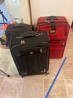 Three pieces of nylon soft side luggage: two black, one red, arranged on tiled floor.