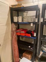 Full view of black plastic snap apart shelf unit in basement area with miscellaneous items on shelves not included in sale.