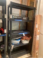 Full view of the black plastic snap-apart shelving unit with four slotted shelves, displaying various unrelated items on shelves (not included).