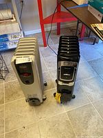 Two electric space heaters placed on a tiled floor; DeLonghi heater off-white, Honeywell heater black and silver.