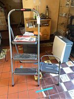 Two folding step stools shown in a kitchen environment. One three-step stool with black steps, and one single-step COSCO stool.