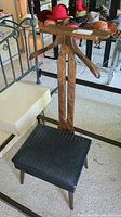 Front view of the wooden men's valet with black vinyl seat showing the hanger and padded seat with vinyl cover in torn condition.
