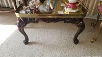 Full view of vintage coffee table with brass top showing carved wooden legs and some items placed on top for illustration only, which are not included.