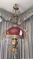 Full view of vintage hanging lamp showing brass frame, red glass shade with floral etching, and hanging crystal prisms.