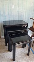 Three vintage black lacquered nesting tables stacked together showing size variation and condition.