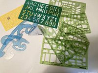Set of various drafting templates, stencils, French curves and a protractor laid out on white surface.