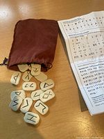 Photo of irregularly shaped light-colored rune blocks with runic symbols next to reddish-brown drawstring bag on wood surface