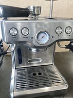 Front view of stainless steel Breville espresso machine showing power and program buttons, pressure gauge, drip tray