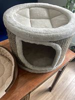 Cat house bed showing circular top sleeping area and doorway to interior space, all lined with soft beige plush fabric with textured scratching exterior on the sides.