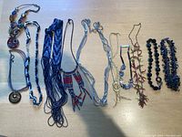 Photo showing full assortment of 11 assorted costume jewelry necklaces with various materials and colors laid out on light wood surface.