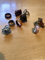Nine costume jewelry rings arranged on a wooden surface showing various designs and colors