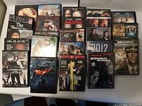 Photo showing mixed DVDs and cases arranged on table, titles visible include The Tourist, Gone Girl, London Has Fallen, The Dark Knight, and others.