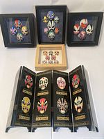 Wide shot showing all four framed mask collections and the small folding screen together on a table.