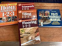 Five paperback how-to books for home improvement and repairs on a wooden surface.