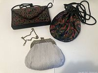 Three ladies handbags shown together: one with pleated white satin and metal frame, one beaded rectangular black handbag, and one beaded round pouch handbag.