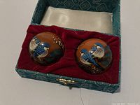 Pair of brown Chinese meditation balls with hand-painted blue and white birds, displayed in red velvet-lined section of a decorative box