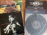 Mixed vinyl records from different artists including Joan Baez cover with black and white image, Judas Priest, Bob James, Dale Jacobs, Atlanta Rhythm Section, Chariot of Fire soundtrack, and Rush vinyl single.
