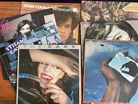 Photo of multiple used vinyl LP album covers including The Cars, Prism, John Cougar, Rod Stewart, Pam Rose, Pat Benatar, and Stray Cats.