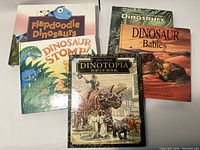 Five dinosaur-themed pop-up books stacked showing front covers with titles visible.