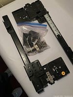 Photo showing metal sliding door tracks, brackets, and a plastic bag with mounting hardware on a white surface.