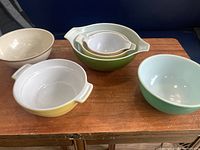 First photo showing all six vintage bowls arranged on a wooden surface, includes the nested Pyrex set plus three other bowls
