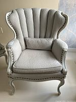 Front view of grey-blue channel upholstered armchair showing fabric detail and decorative metal pins on wood frame.
