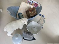 Blue metal wire basket with plastic wrapping, white resin lamb figurine, ceramic dish, vintage metal iron, decorative tin, floral placemats/runner visible in angle