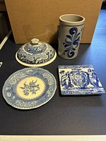Top view of the four items: ceramic lid, vase, trivet, and plate on a dark surface