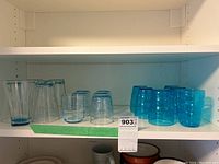 Shelf with all glasses grouped by size: five tall clear blue glasses, six small clear glasses, six medium blue ribbed glasses