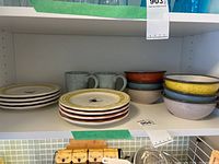 Various bowls including yellow, orange, blue, grey speckled, stacked with 2 pairs of matching grey mugs and small plates