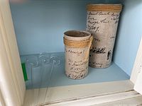Pair of glass candle holders wrapped in fabric and tied with rope alongside three clear glass spike tea light holders on a white shelf