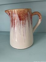 Front and side views of ceramic pitcher showing ombré red to cream glaze, handle, and spout
