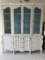 Front view of white distressed chalk painted china cabinet with four glass doors and blue interior, showing upper glass display and lower drawers and cabinets.