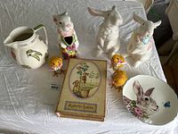 Overview of all Easter-themed porcelain and ceramic items laid out on cloth: 2 rabbits, 3 chicks, pitcher, plate, and decorative box.