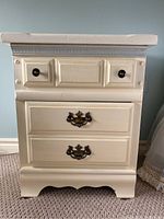 Front view of vintage cream colored nightstand showing two drawers with different handles and knobs.