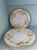 Three Noritake dessert plates stacked showing floral and gold design on cream background.