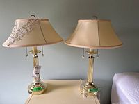 Pair of brass table lamps on a table; beige shades, one with lace and beads embellishment